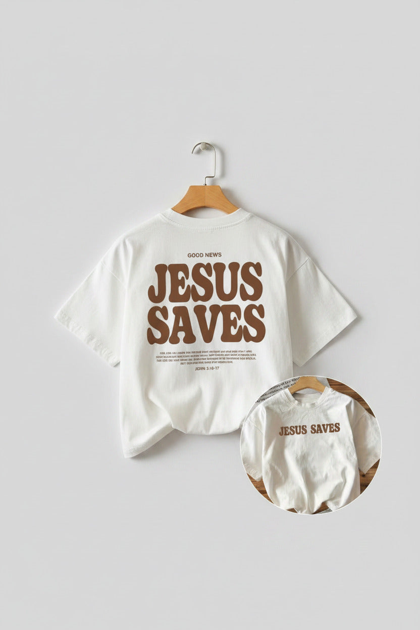 White t-shirt with 'Jesus Saves' text on a wooden surface with a baby onesie and sneakers.