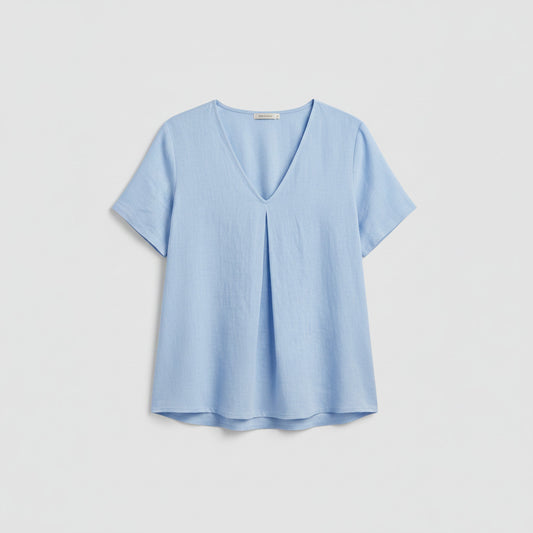Person wearing a light blue shirt and ripped jeans indoors.