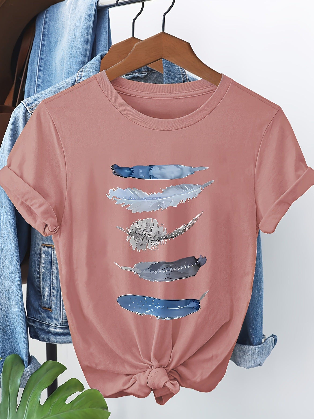 Pink t-shirt with abstract blue designs on a hanger against a denim background