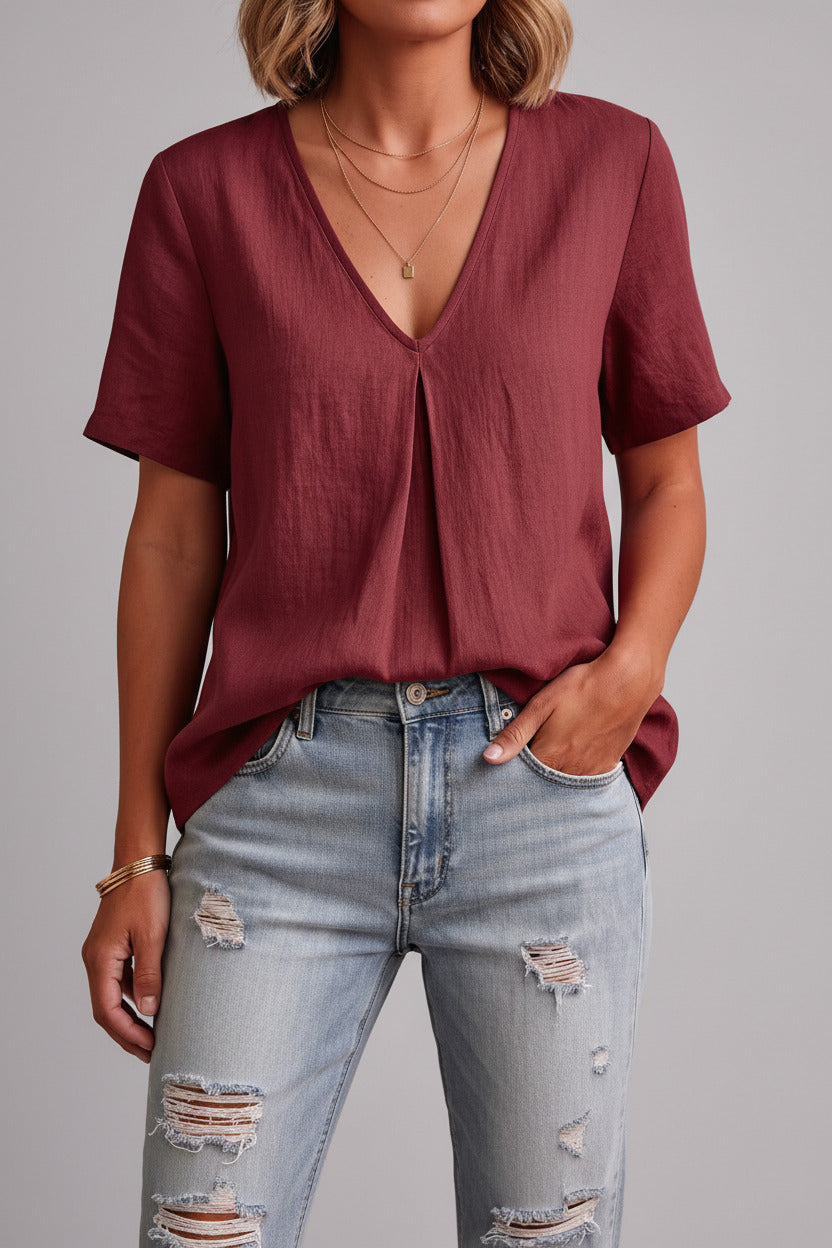 Person wearing a burgundy shirt and ripped jeans indoors