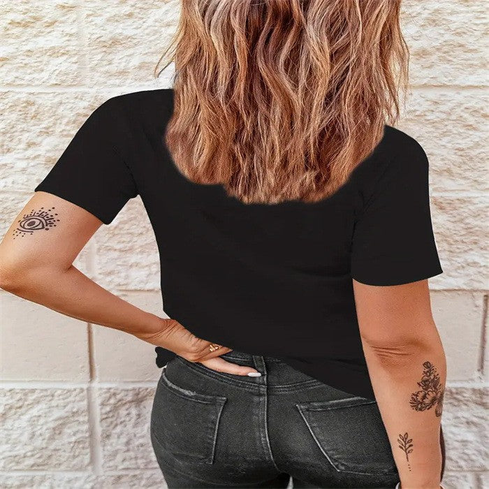 Person wearing a black t-shirt and dark jeans with tattoos on arms against a stone wall.