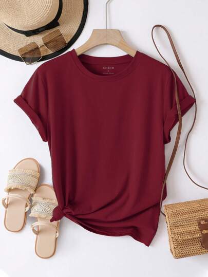 Maroon t-shirt on a hanger with sandals, hat, and bag on a white background