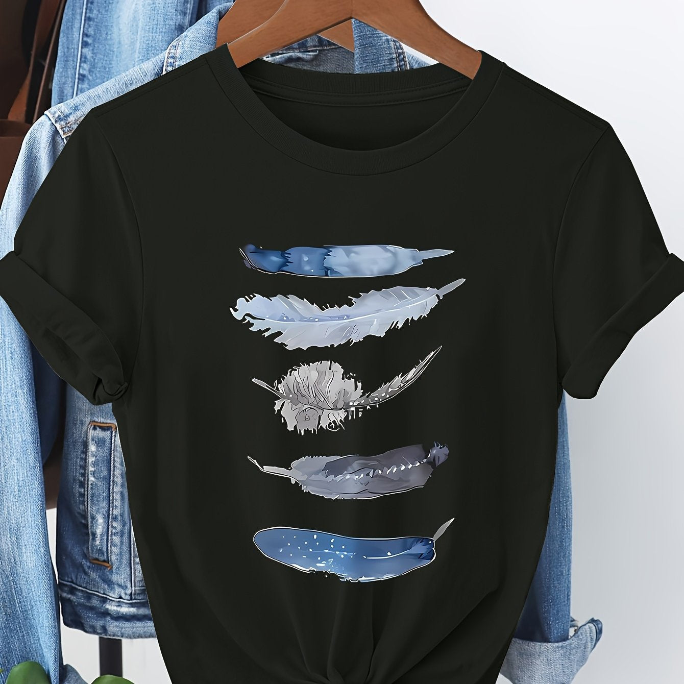 Black t-shirt with feather design on a hanger against a denim background