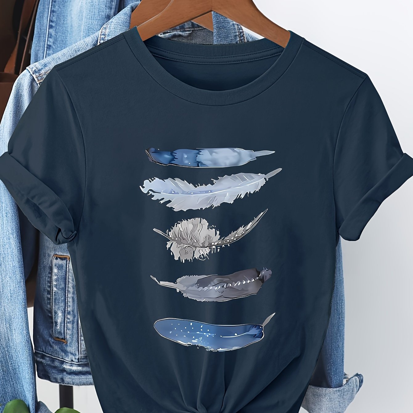 Navy blue t-shirt with feather designs on a hanger against a denim background