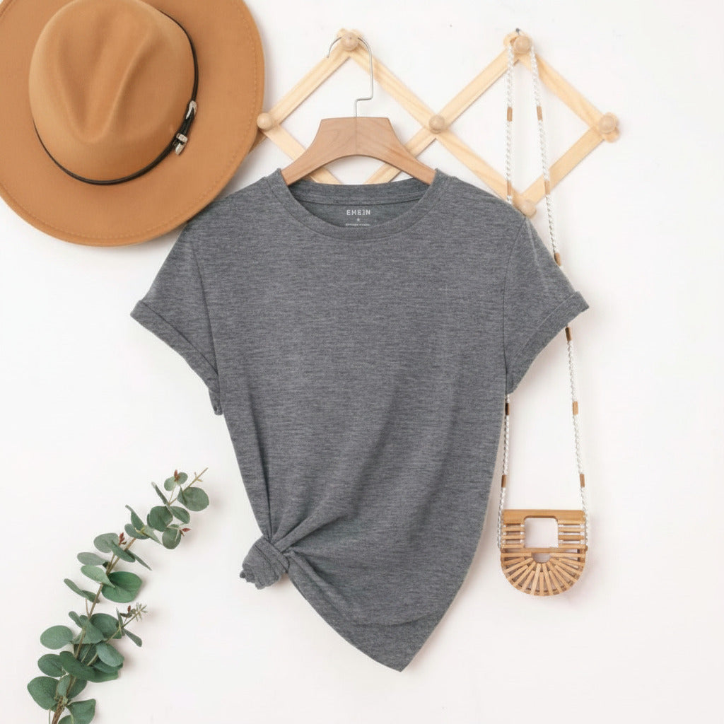 Gray t-shirt with a knot detail on a hanger, surrounded by a hat, plant, and bag on a white background