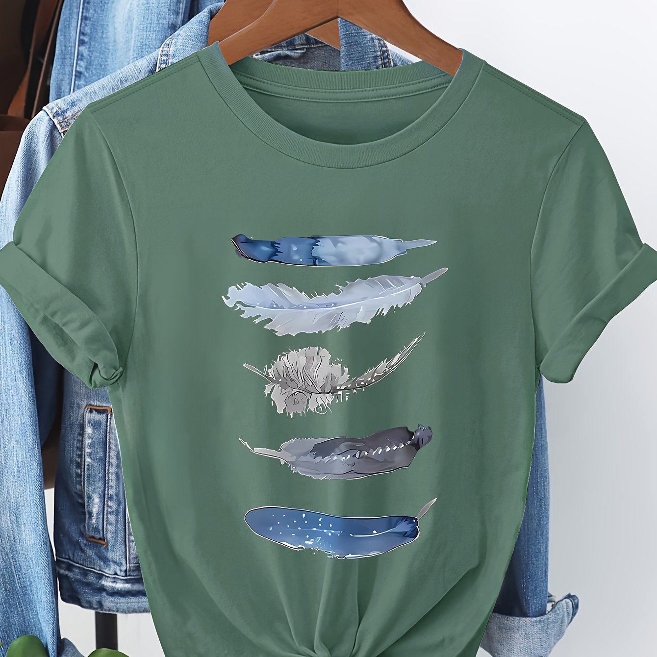 Green t-shirt with feather design on a hanger against a denim background