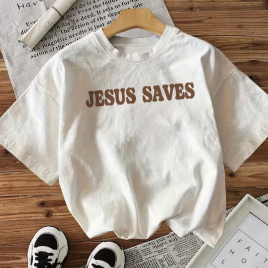 White t-shirt with 'JESUS SAVES' text on a wooden surface with shoes and newspaper.
