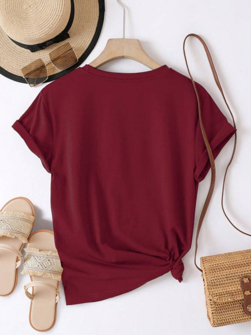 Maroon t-shirt on a hanger with a straw hat, sandals, and bag on a white background