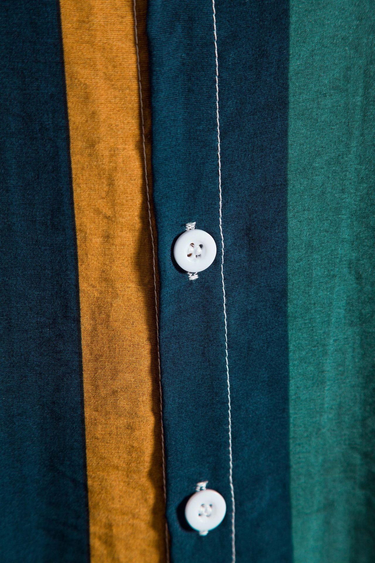 Close-up of a shirt with vertical stripes in blue, brown, and green, featuring a button.